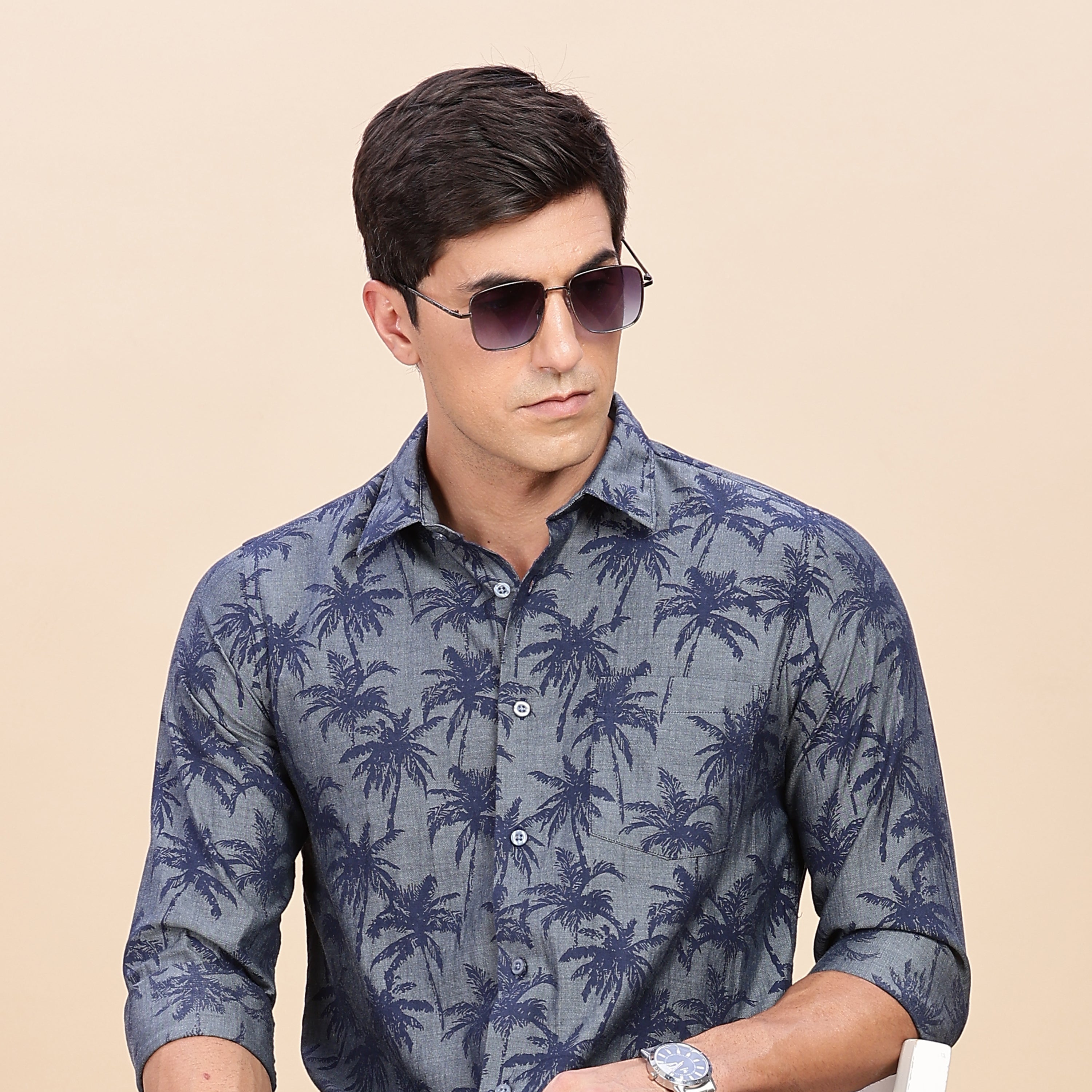 Man wearing a blue patterned shirt sitting on a white chair against a beige background