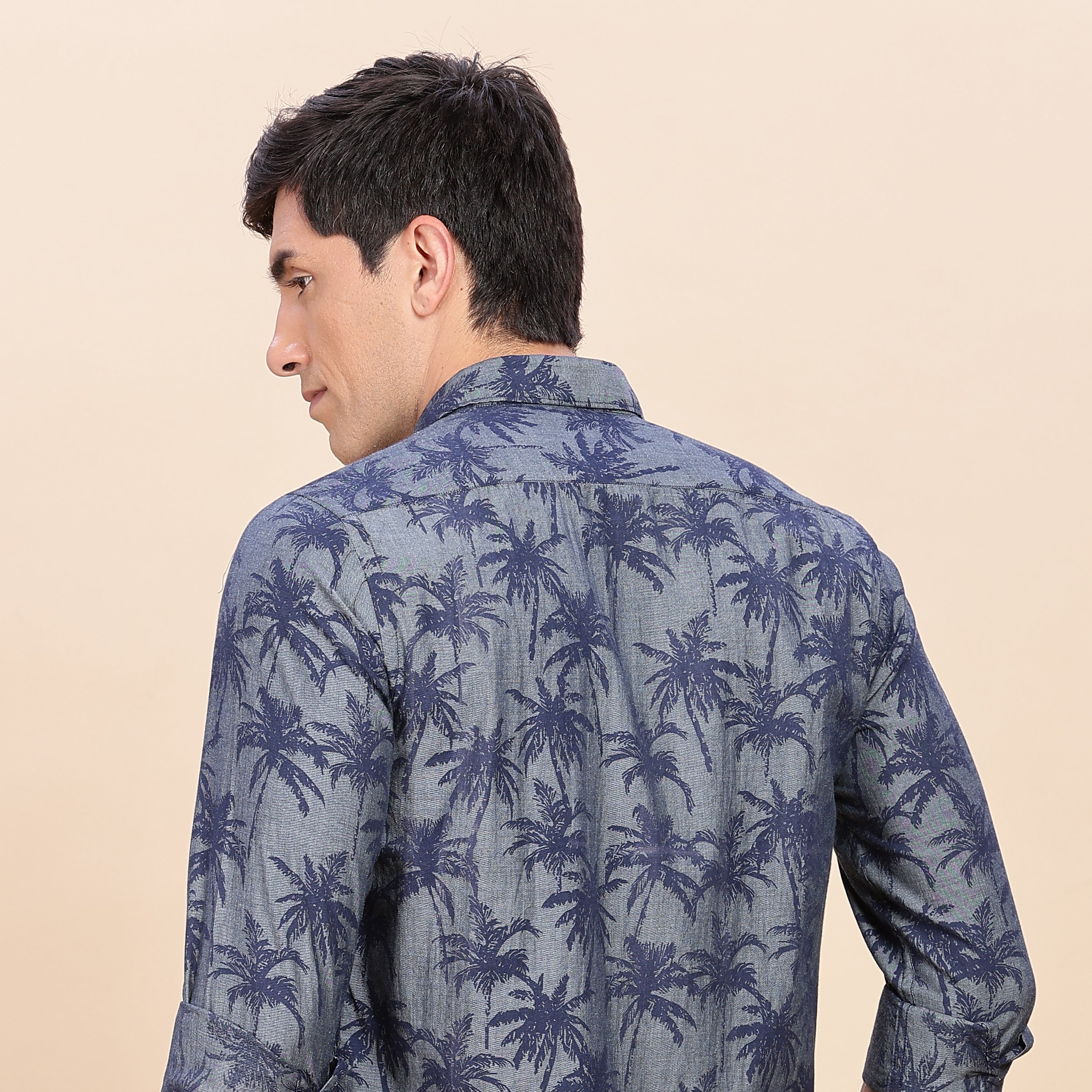 Man wearing a blue palm tree patterned shirt on a beige background